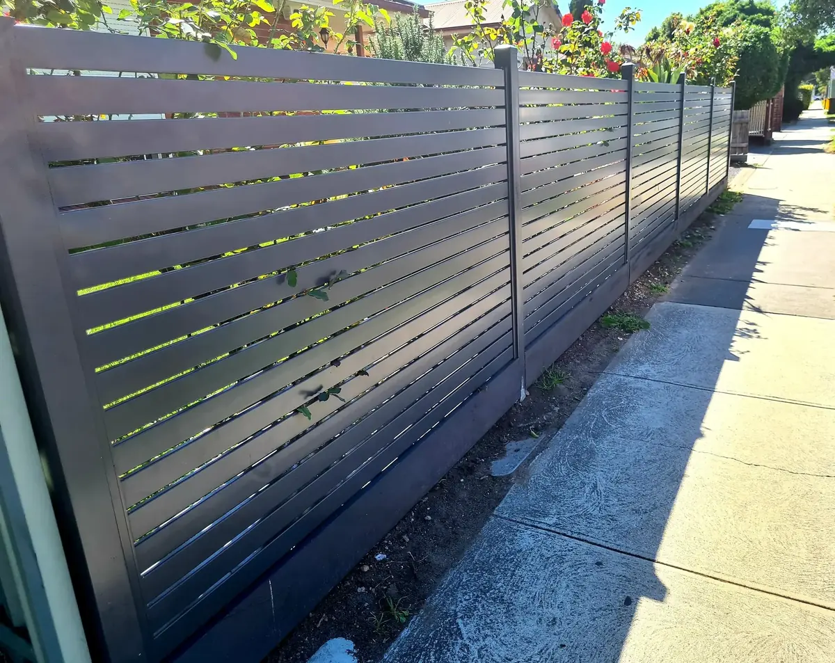 Long charcoal horizontal slat boundary fence following a suburban property line